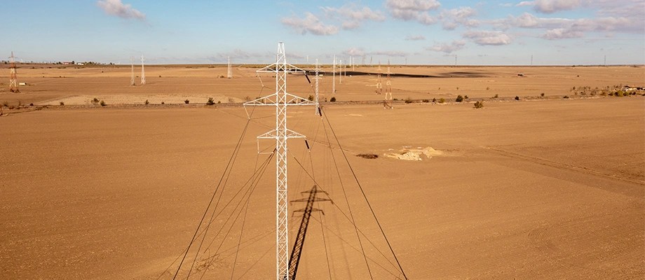Stâlpi de înaltă tensiune într-o zona agricolă întinsă.