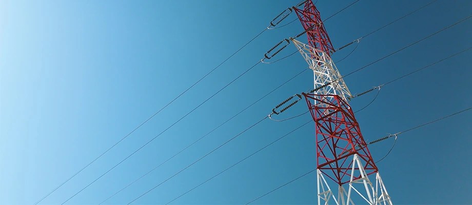 Stâlp de înaltă tensiune vopsit în roșu și alb, pe un fundal de cer albastru.