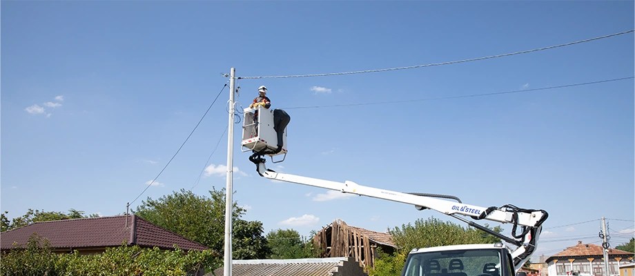 Electrician in an aerial lift, performing maintenance work on the power grid in a rural area.