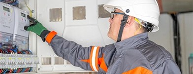 Tehnician electric verificand un contor inteligent intr-un panou de distributie