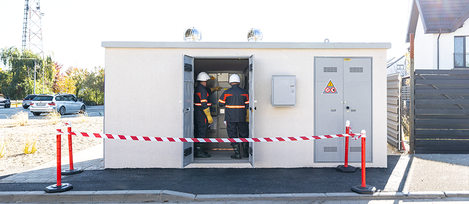 Two technicians in work gear enter a compact transformer station.