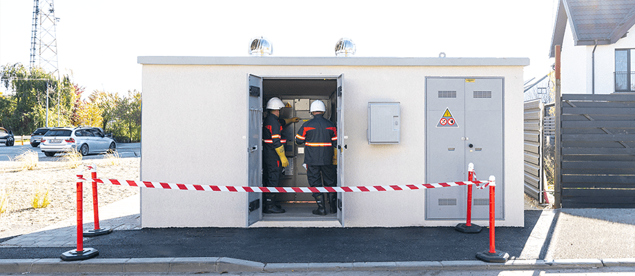 Two technicians in work gear enter a compact transformer station.