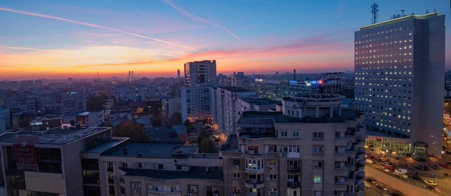 Panorama a unui oras la apus, cu cladiri inalte si strazi iluminate