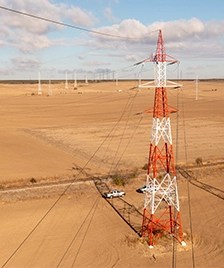 Stalp de inalta tensiune rosu si alb intr-un peisaj arid, cu linii electrice extinzandu-se in departare.