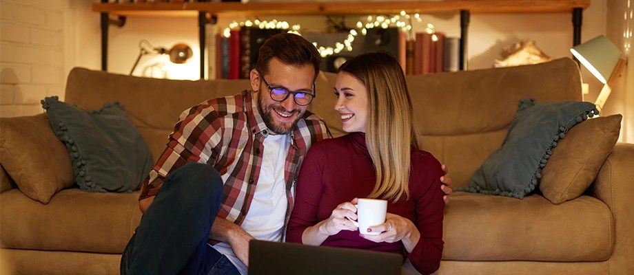 Cuplu care se relaxează într-un living confortabil, iluminat ambiental.